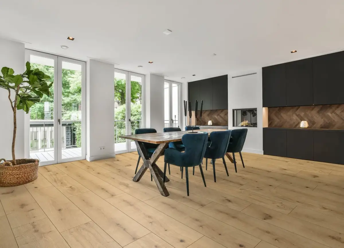 Nowoczesne wnętrze z drewnianą podłogą, idealne do układanie paneli. Stół z krzesłami i kominek tworzą przytulną atmosferę.