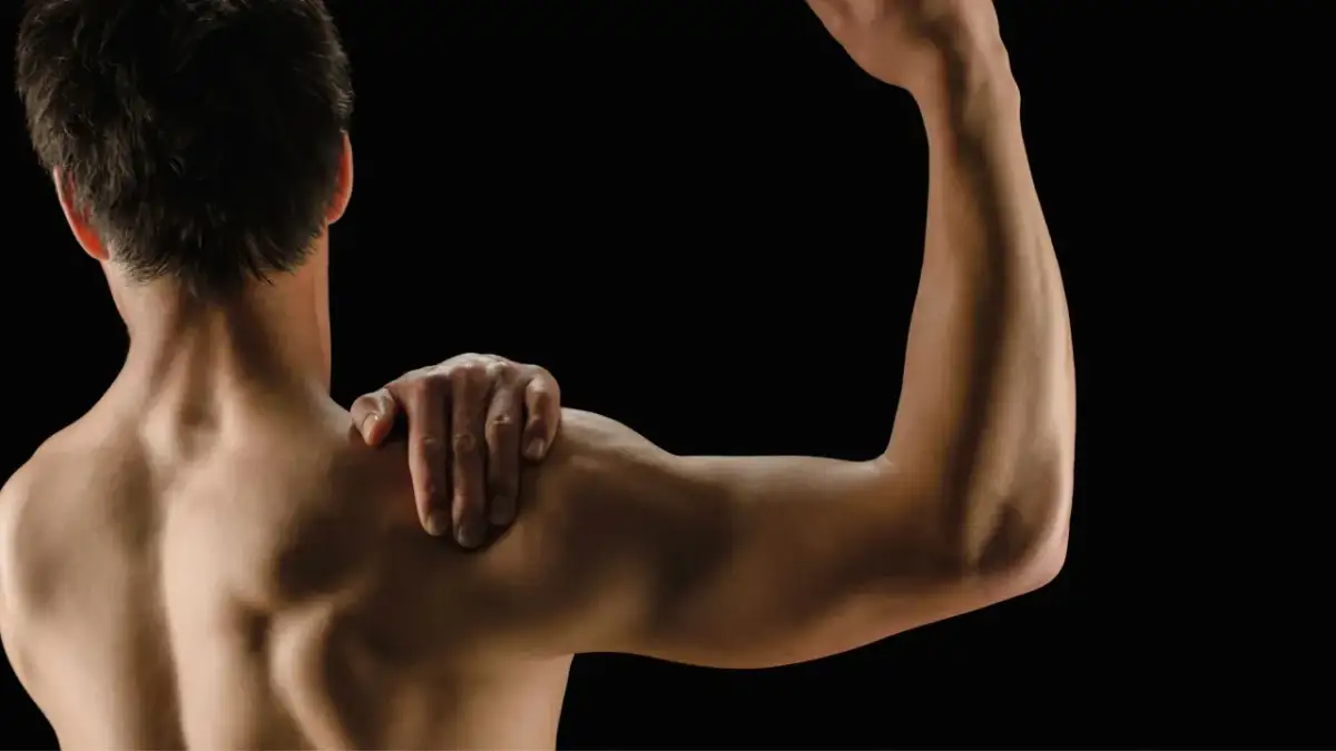 Mężczyzna z ręką na ramieniu, pokazujący umięśnione plecy i biceps. Białko po treningu wspiera regenerację mięśni.