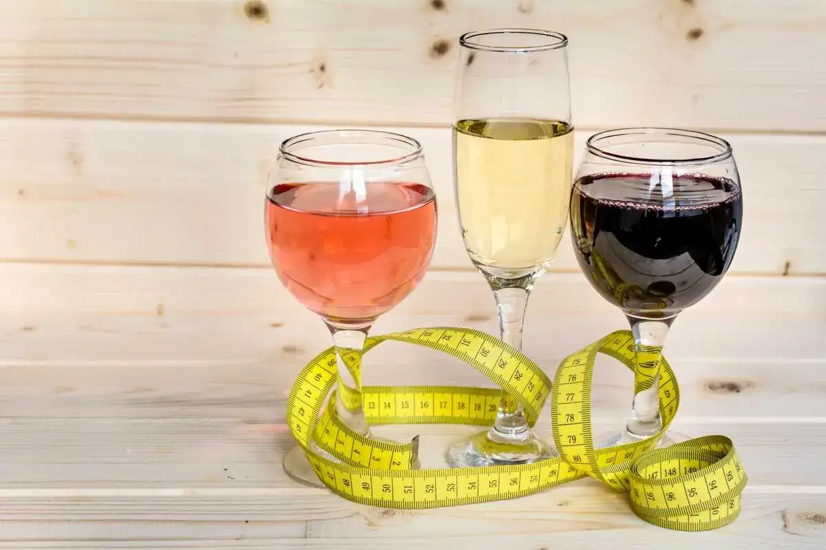 Trzy kieliszki z winem (różowym, białym, czerwonym) i miarka krawiecka. Zastanawiasz się, ile kcal ma pół litra wódki?