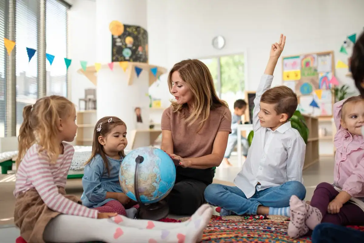 Nauczycielka z dziećmi przy globusie. Dzieci uczą się o świecie, zastanawiając się, ile kosztuje przedszkole publiczne.