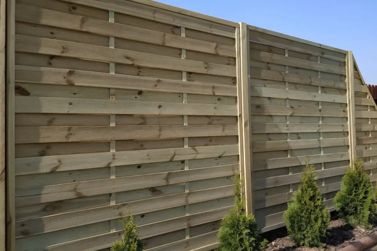 Drewniany płot lamelowy, idealny przykład jak zamontować plot lamelowy. Widać poziome deski i pionowe słupki.