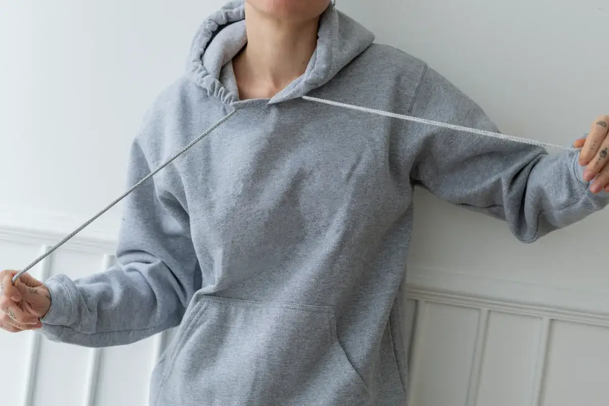 Osoba pokazuje, jak zawiązać sznurki w bluzie, trzymając je w dłoniach.