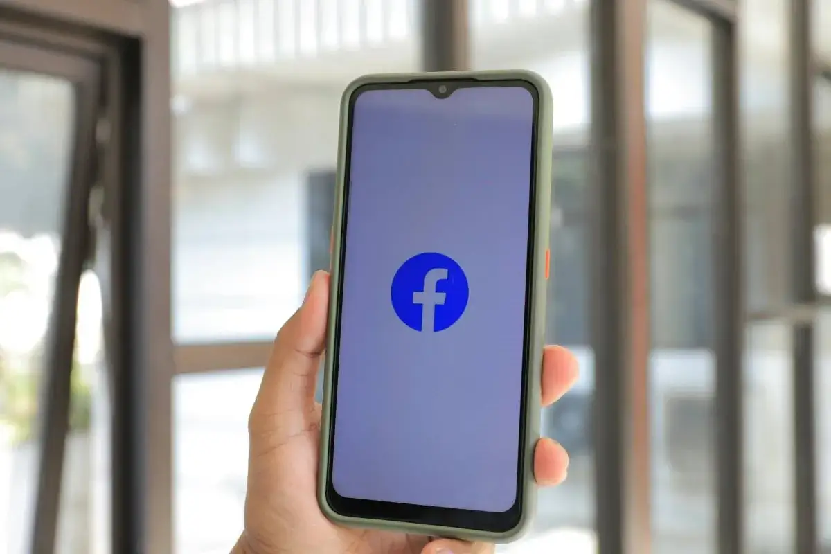 Dłoń trzyma smartfon z logo Facebooka. Chcesz wiedzieć, jak wyłączyć urodziny na FB?