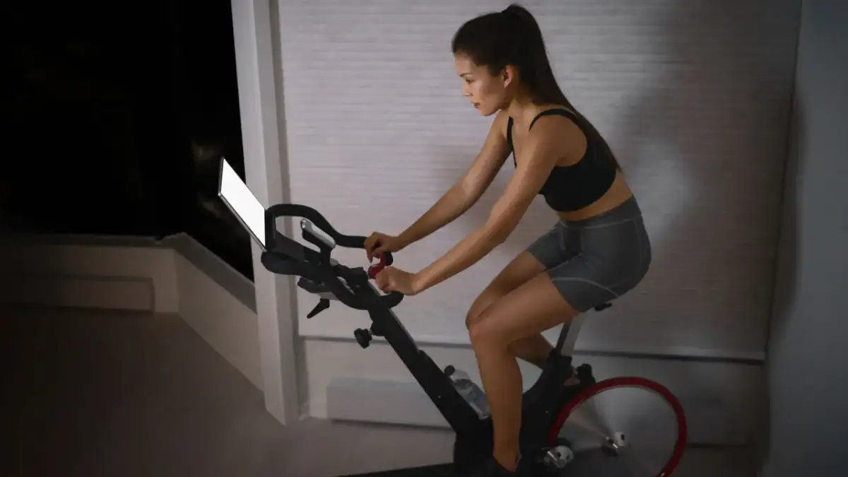 Kobieta ćwiczy na rowerze stacjonarnym, zastanawiając się, czy na rowerze stacjonarnym można schudnąć.