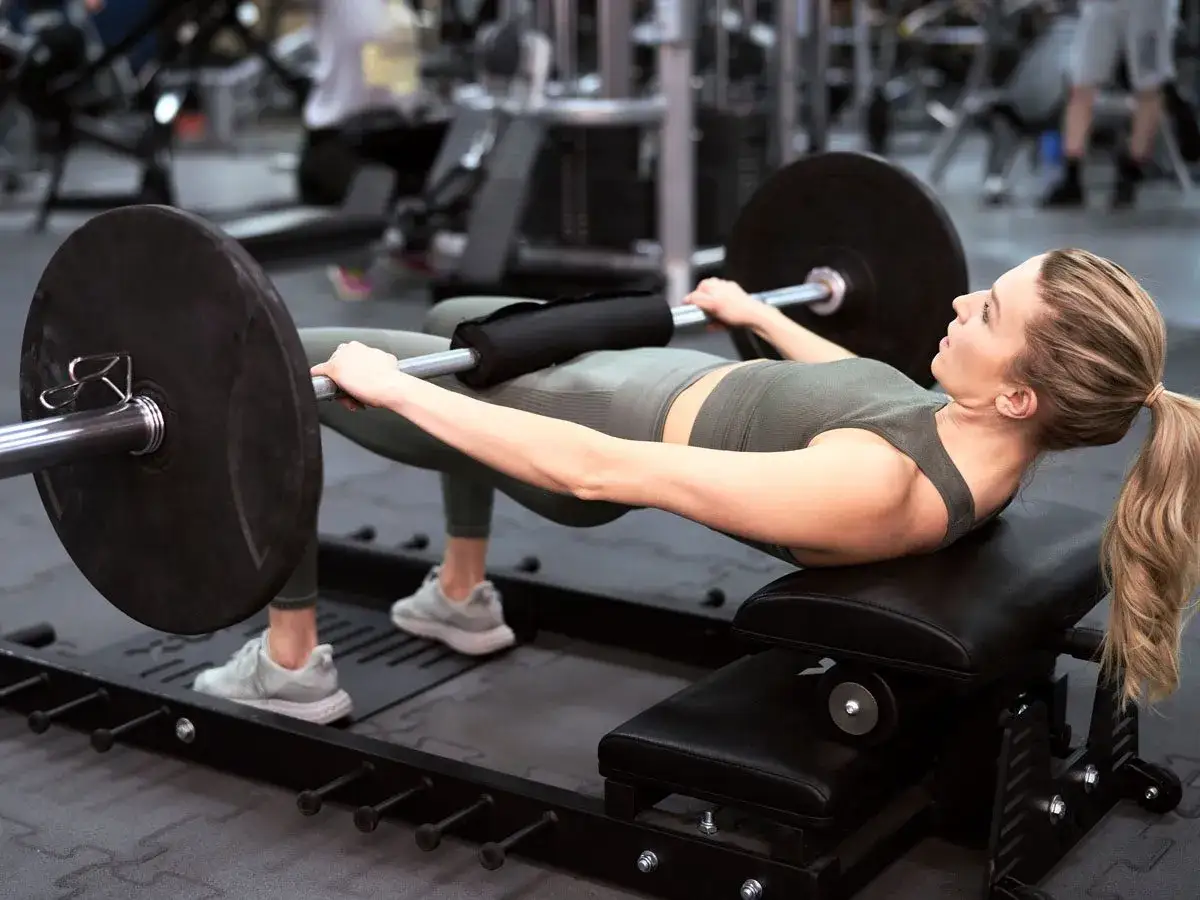 Kobieta wykonuje hip thrust z obciążeniem na ławce. Ćwiczenie to świetnie wzmacnia pośladki i jest możliwe do wykonania nawet w domu.