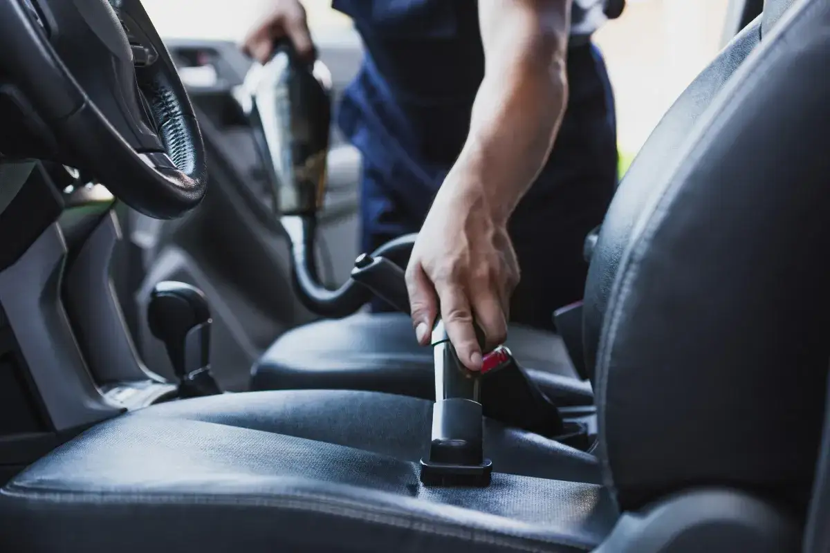 Osoba odkurza siedzenie samochodu, dbając o czyszczenie wnętrza.