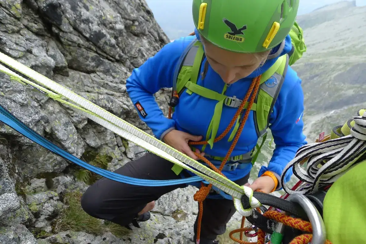 Dziewczyna w kasku i sprzęcie wspinaczkowym przygotowuje się do wspinaczki. To pierwszy krok, jak zostać taternikiem.