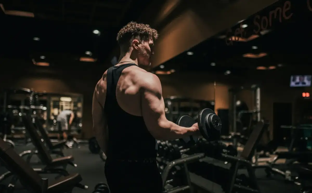 Mężczyzna ćwiczy biceps z hantlem w siłowni. To dowód, jak crossfit zmienił moje życie, budując siłę i pewność siebie.