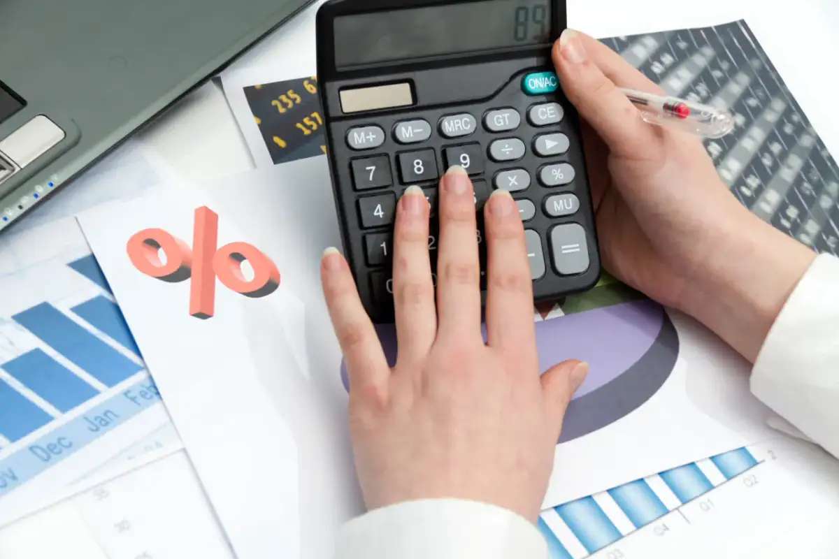 Ręce na kalkulatorze, obok wykresy i symbol procentu. Przykład: jak obliczyć odsetki od pożyczki.