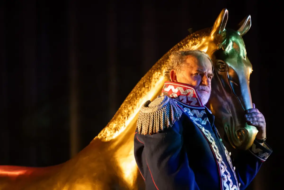 Starszy mężczyzna w mundurze, jak z epilogu "Pana Tadeusza", trzyma złotą głowę konia.