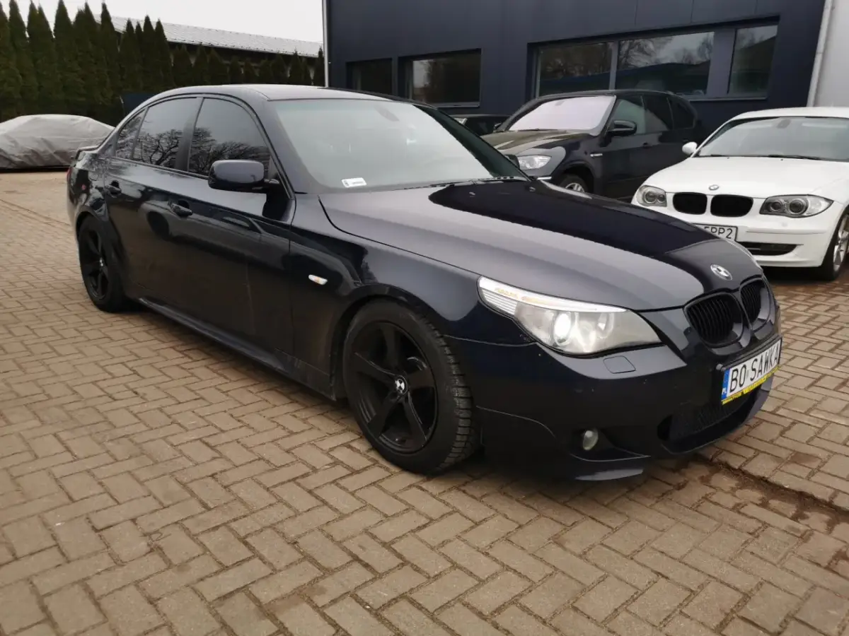 Ciemnogranatowe BMW E60 535d na czarnych felgach, zaparkowane na kostce brukowej przed budynkiem.