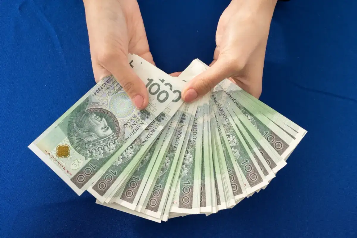 Ręce trzymają wachlarz banknotów 100 zł. Zastanawiasz się, ile dać na 18 urodziny chrześnicy?