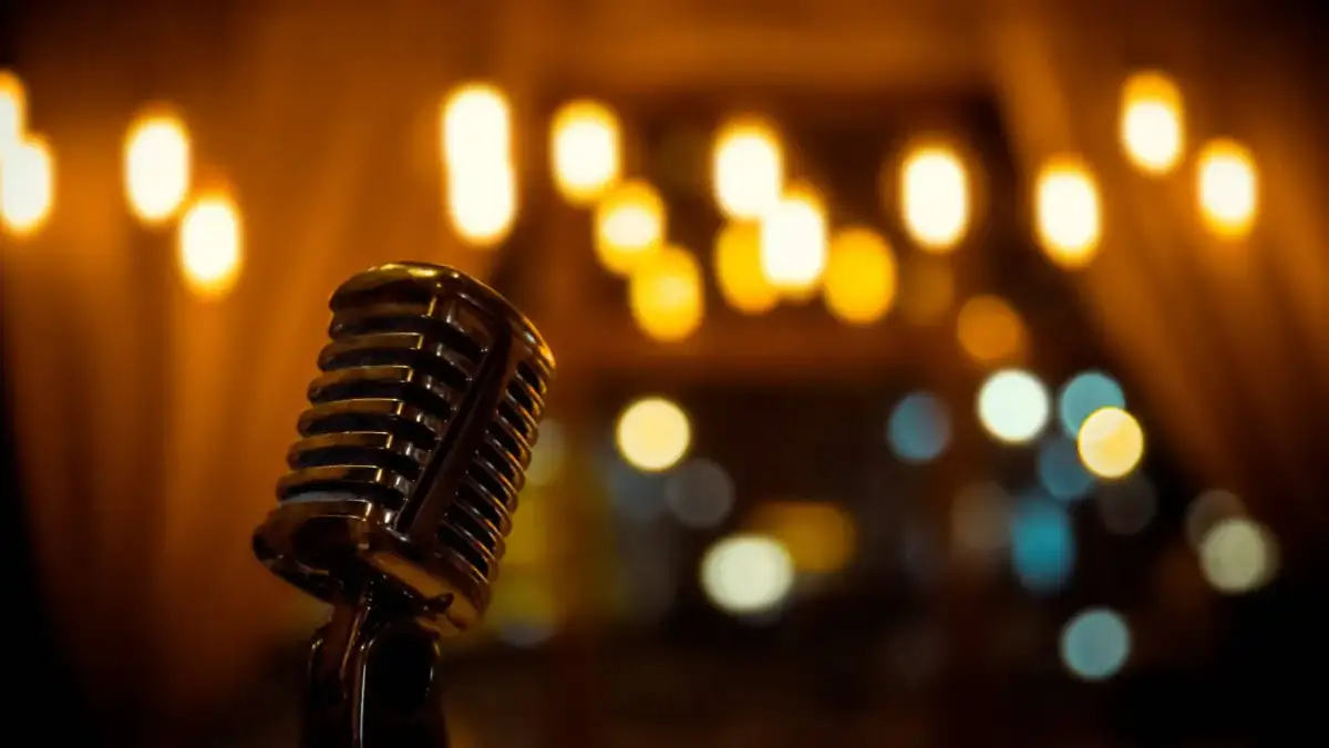 Stary mikrofon na statywie, gotowy do występu. W tle ciepłe, rozmyte światła.