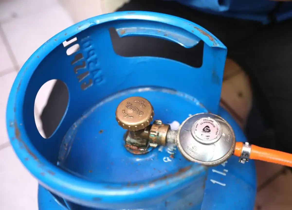 Niebieska butla z gazem, z widocznym reduktorem i pomarańczowym wężem. Wygląda na to, że nie można zakręcić butli z gazem.