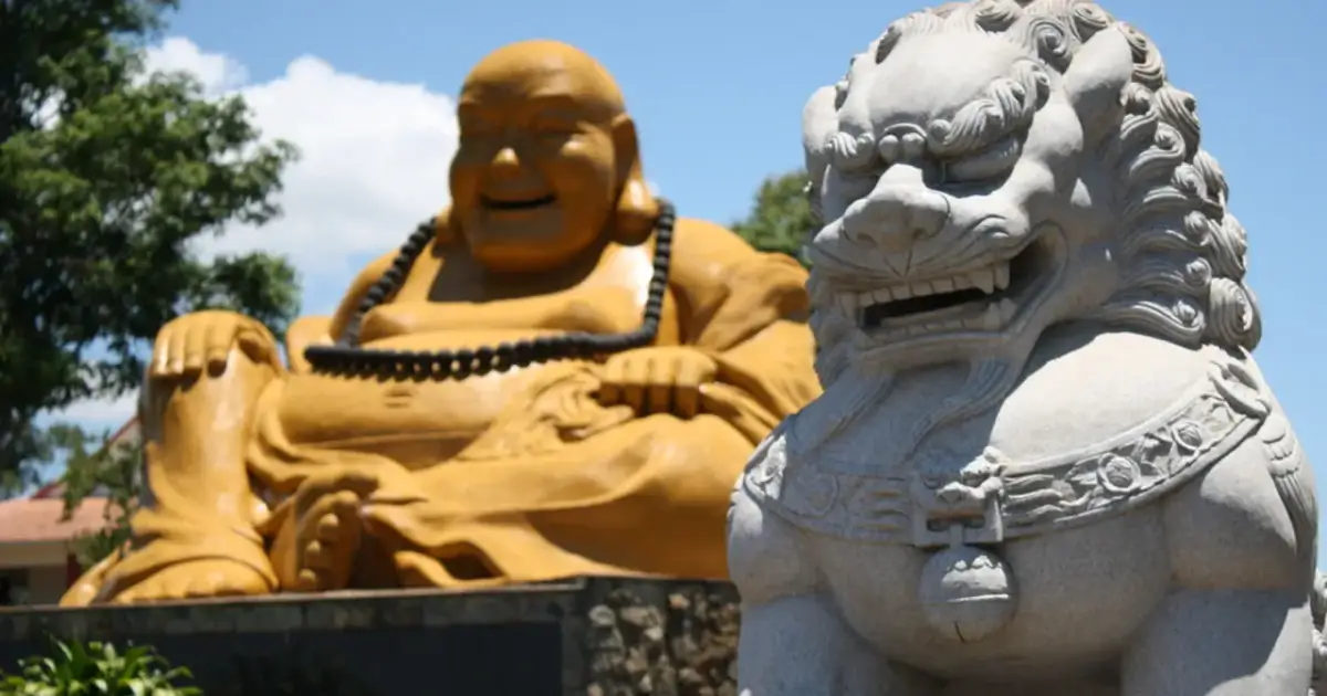 Złoty Budda i kamienna lwica strażniczka na tle błękitnego nieba.