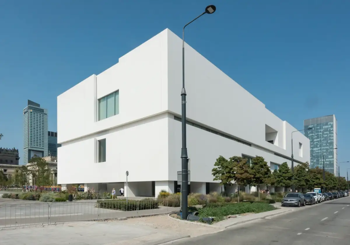 Nowoczesny budynek Muzeum Sztuki Nowoczesnej w Warszawie, projekt architektoniczny o białej fasadzie, na tle błękitnego nieba.