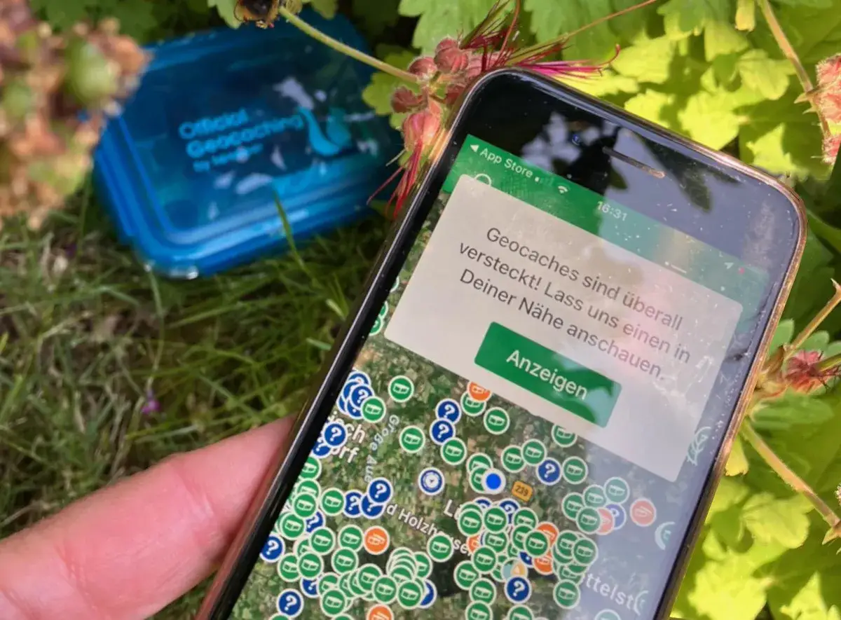 Smartfon pokazuje mapę z zaznaczonymi skrytkami. To jest właśnie geocaching – poszukiwanie ukrytych skarbów.