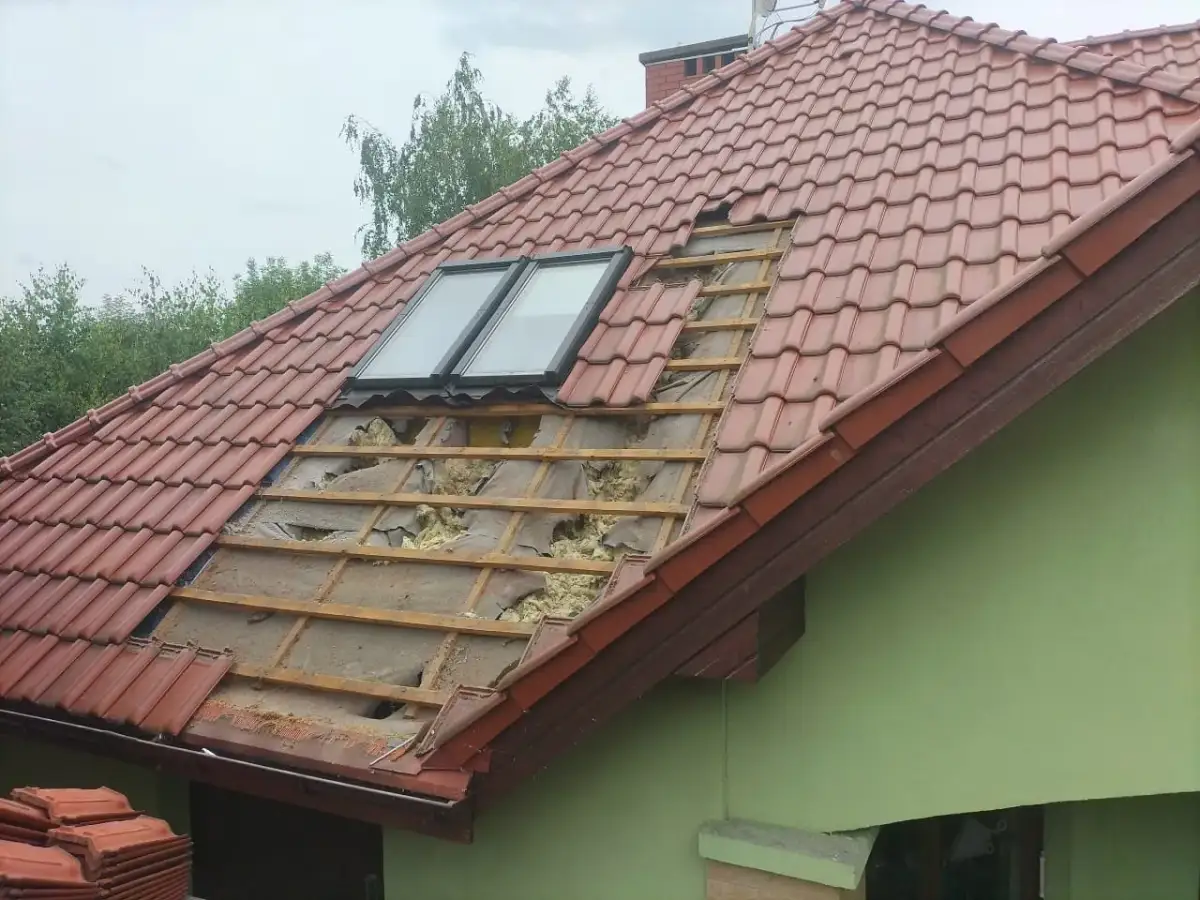 Uszkodzony dach z dachówką, widoczne okna dachowe i izolacja. Czas pomyśleć, jak uszczelnić dach przed kunami.
