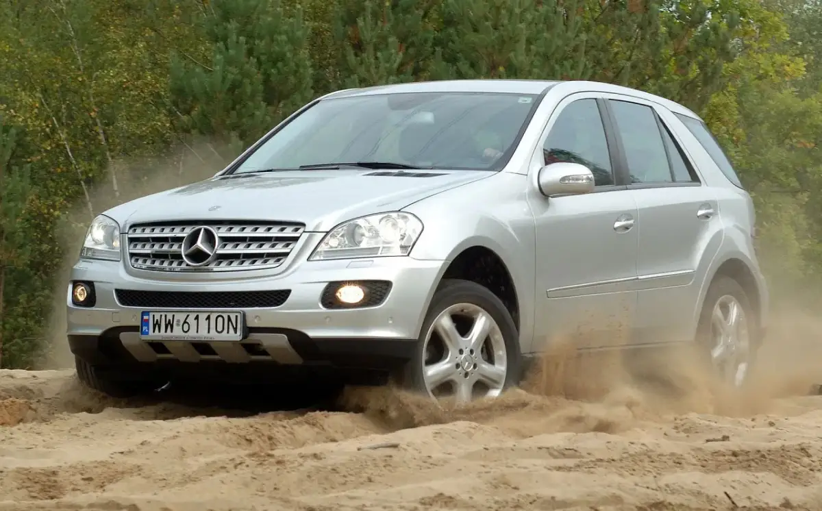 Srebrny Mercedes-Benz M-Class pokonuje piaszczysty teren, wzbijając tumany kurzu.