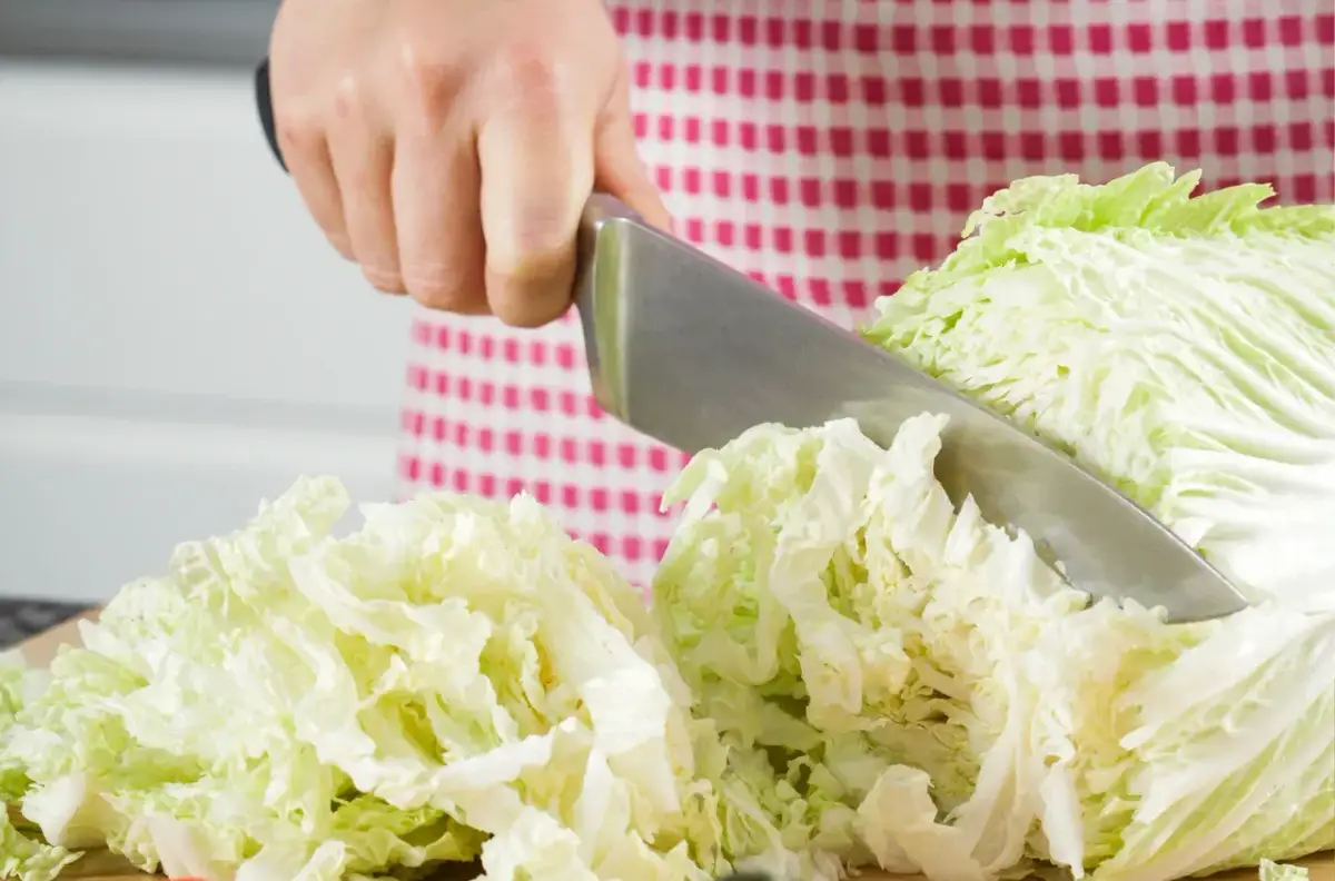Ręka kroi kapustę pekińską na desce. Powstaje pyszna surówka z kapusty pekińskiej.