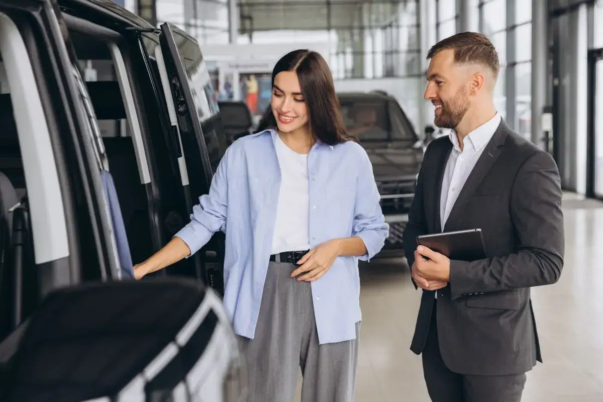 Kobieta ogląda samochód w salonie, sprzedawca z tabletem oferuje leasing bezpośredni.