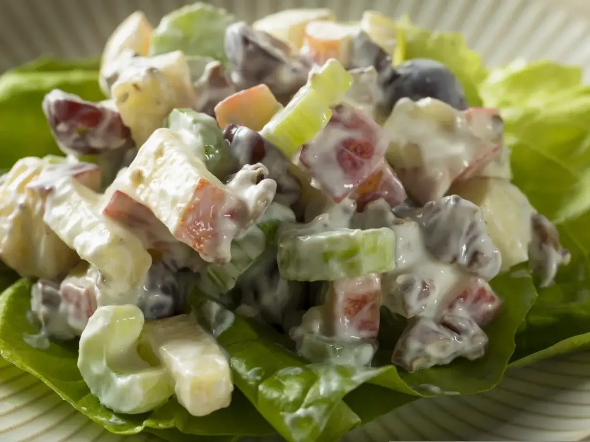 Pyszna sałatka z selera, jabłek, rodzynek i winogron, polana kremowym sosem. Idealna na lekki posiłek.