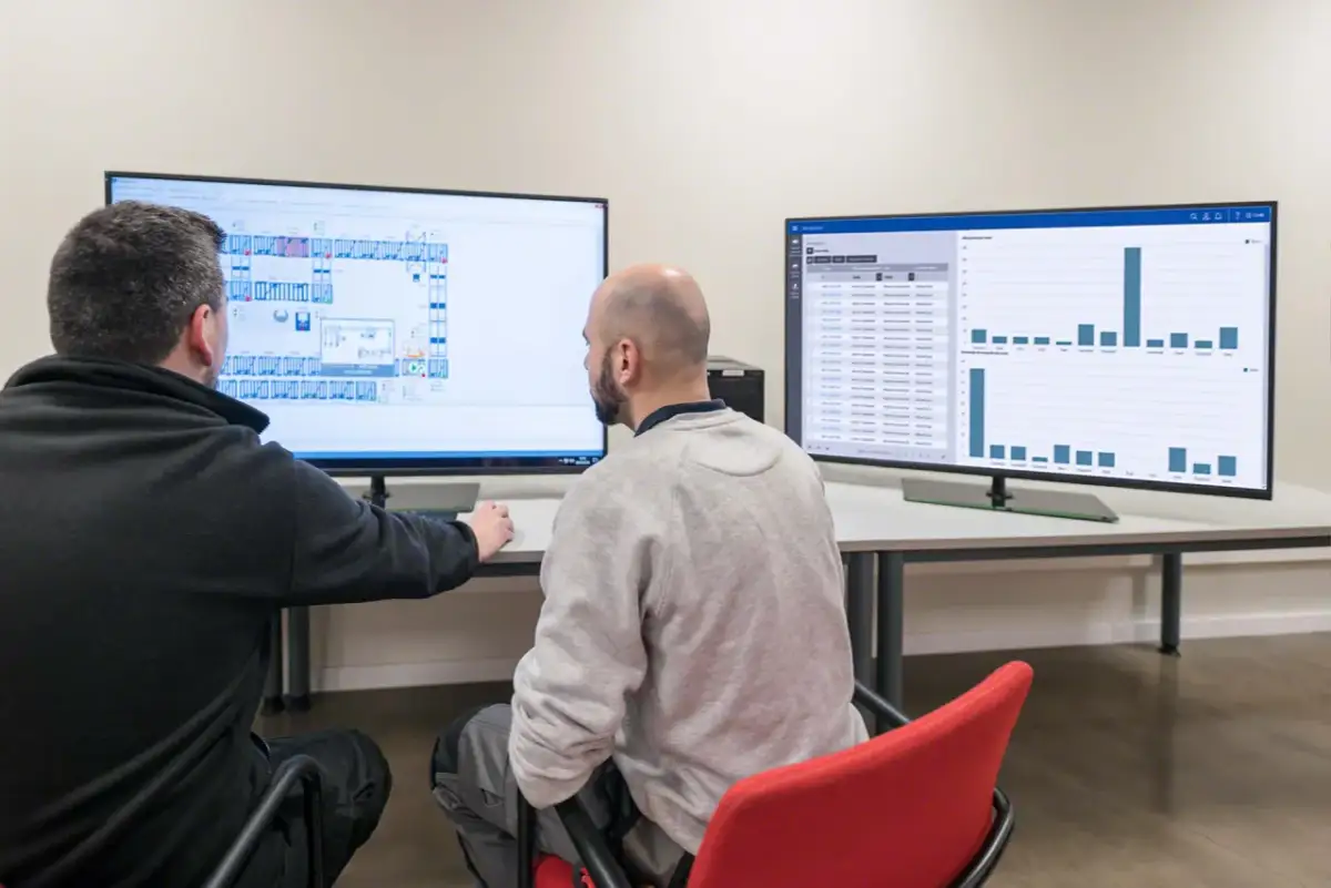 Dwóch mężczyzn analizuje dane na monitorach. Na jednym schemat budynku, na drugim wykresy, które pomagają w prognozowaniu popytu.