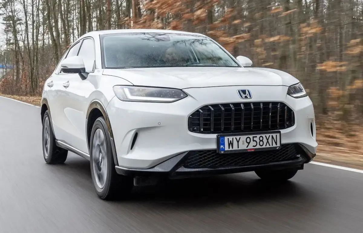 Biały Honda ZR-V jedzie po drodze wśród drzew.