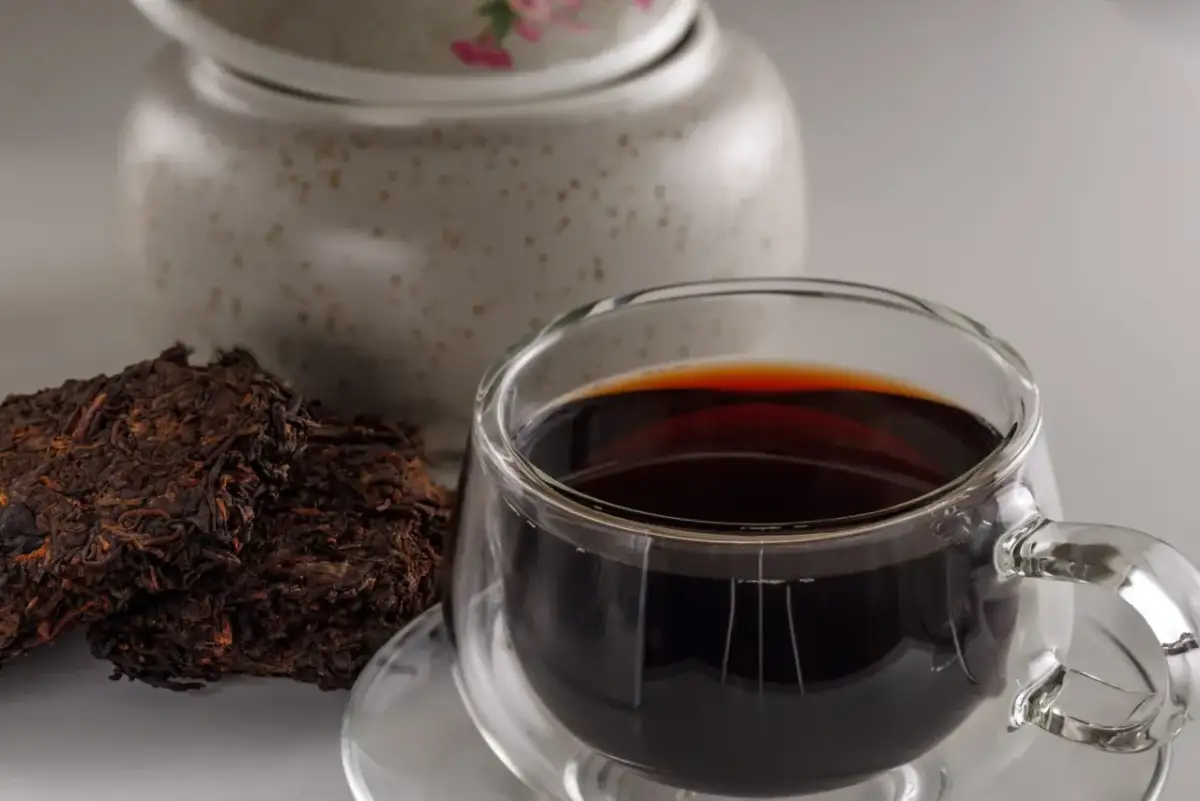 Ciemna, aromatyczna czerwona herbata w szklance, obok sprasowane liście. Odkryj jej niezwykłe właściwości.