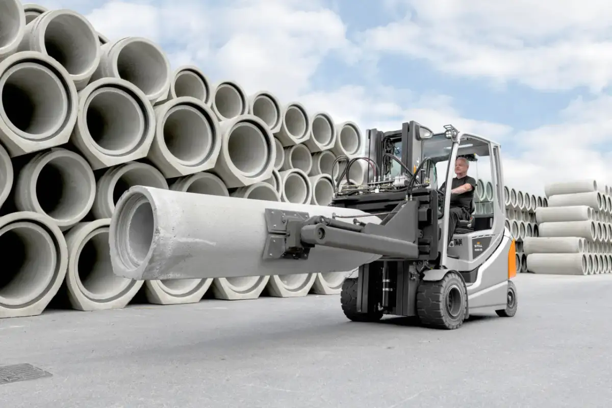 Wózek widłowy z operatorem transportuje dużą betonową rurę. W tle piętrzą się kolejne elementy tej jednostki ładunkowej.