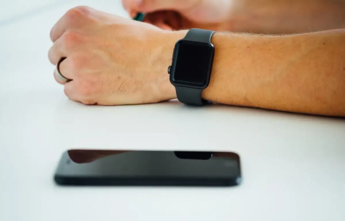 Czarny smartwatch na nadgarstku, obok leży wyłączony smartfon. Co zrobić, gdy smartwatch nie chce się włączyć?