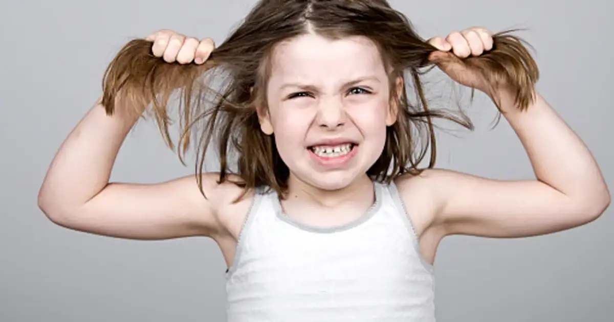 Wściekłe dziecko bije się po głowie, szarpiąc za włosy.