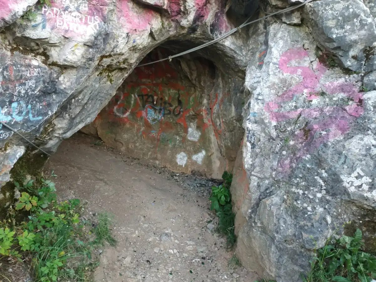 Wejście do jaskini w rezerwacie przyrody Kadzielnia, pokryte graffiti. Stalowa lina biegnie nad wejściem.