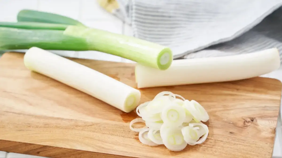 Na drewnianej desce leżą pory, część pokrojona w krążki, gotowa na pyszną surówkę z pora.