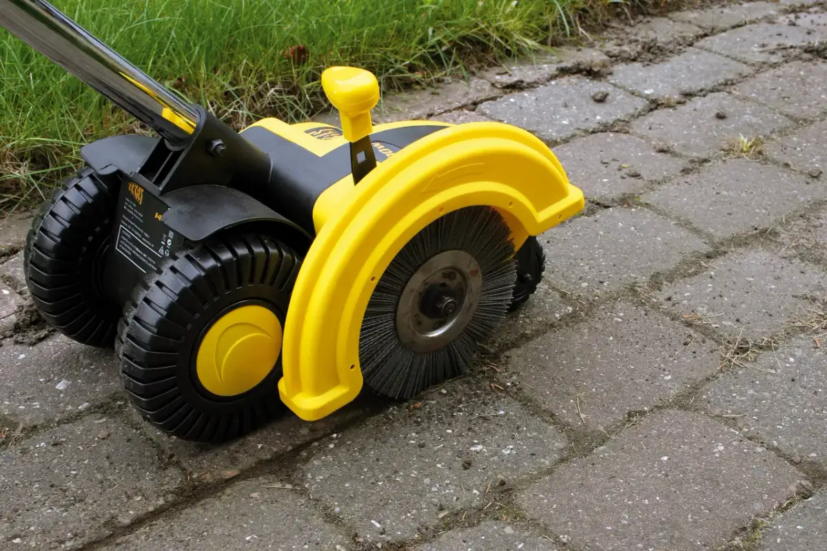 Żółta elektryczna zamiatarka do kostki z czarnymi kołami i szczotką, gotowa do pracy na podjeździe.