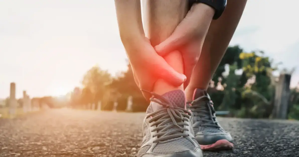 Osoba trzymająca się za bolącą kostkę podczas biegu, z czerwonym zaznaczeniem bólu.