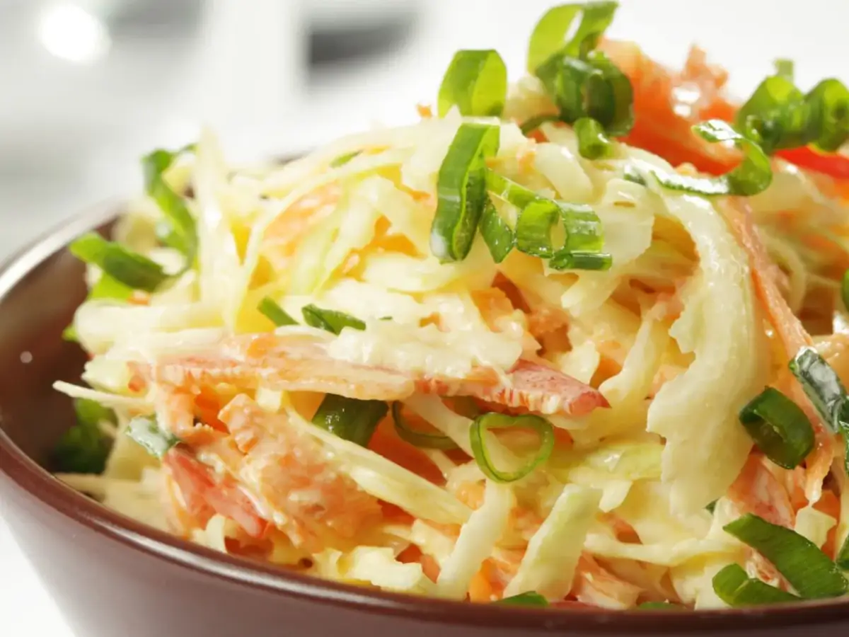 Surówka z białej kapusty i marchewki z zieloną cebulką w brązowej misce.