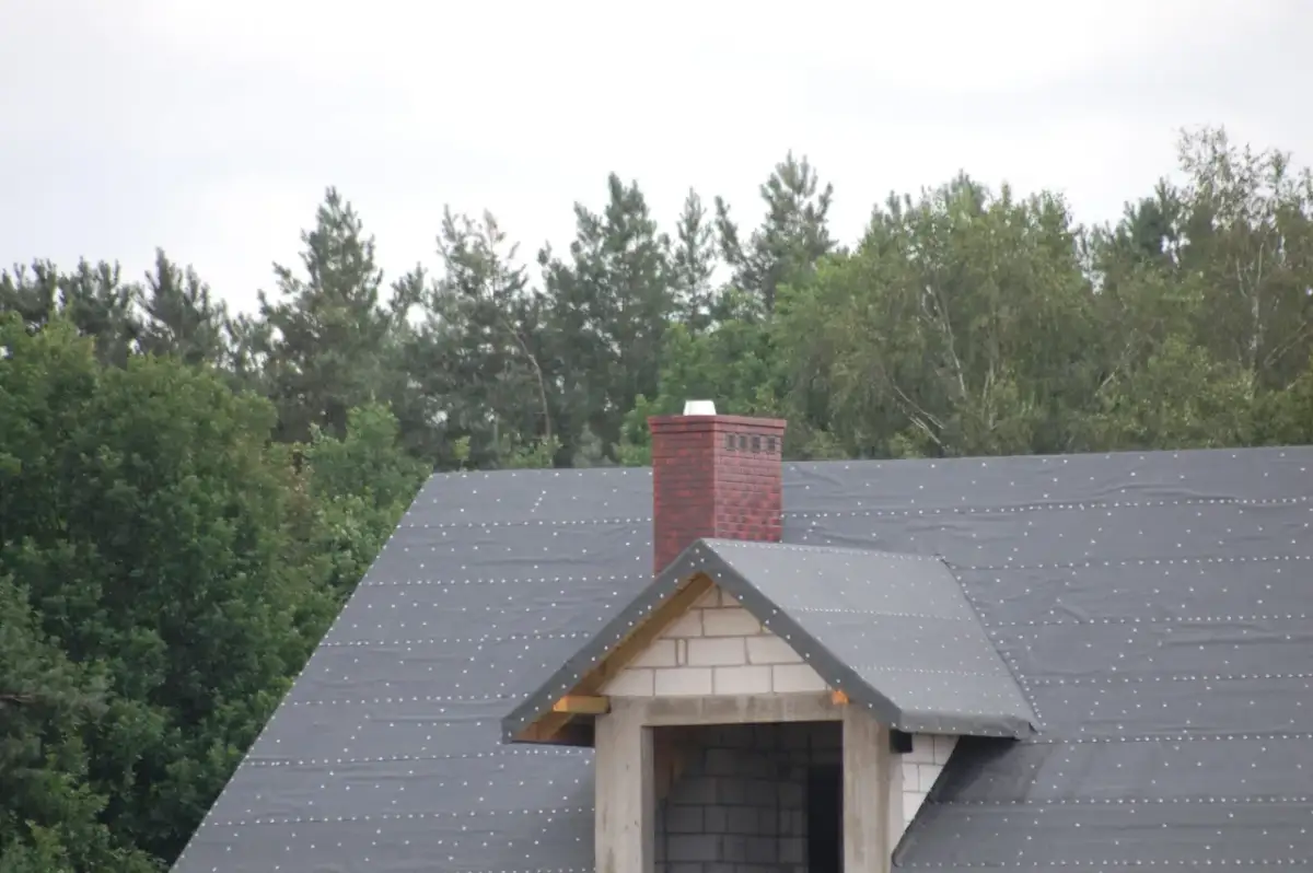 Ceglany komin na dachu w trakcie budowy. Zastanawiasz się, jak naprawić pęknięty komin? Ten obraz pokazuje jego obecny stan.