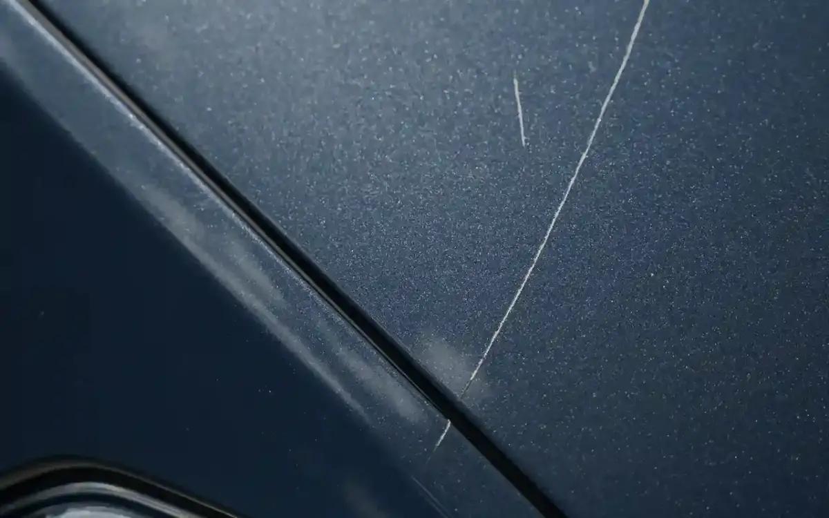 Widoczne rysy na ciemnym lakierze samochodowym, wymagające czyszczenia.