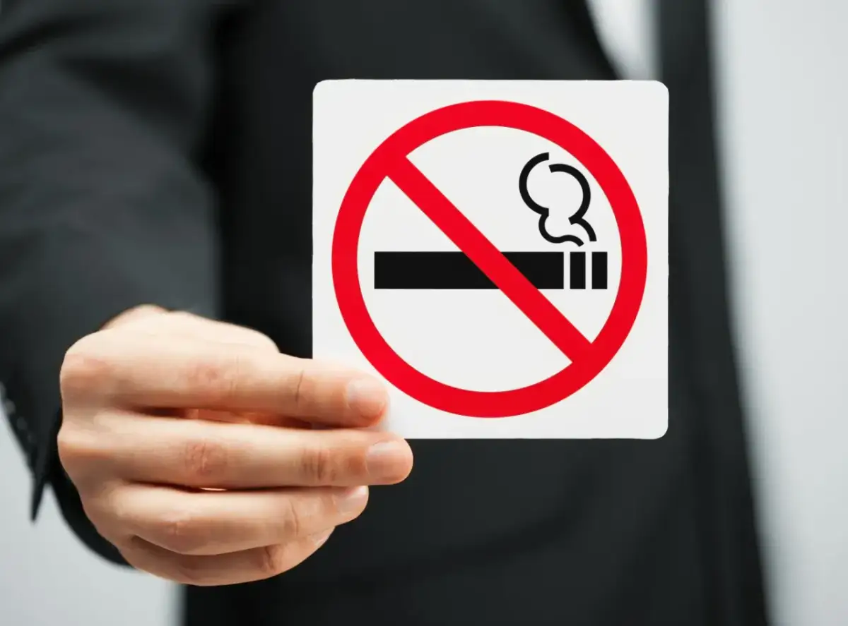 Dłoń w garniturze trzyma tabliczkę z zakazem palenia.