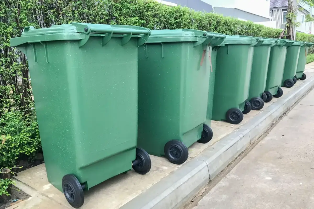 Zielone kosze na śmieci stoją w rzędzie. Segregacja odpadów to klucz do tego, jak uniknąć opłaty za śmieci.
