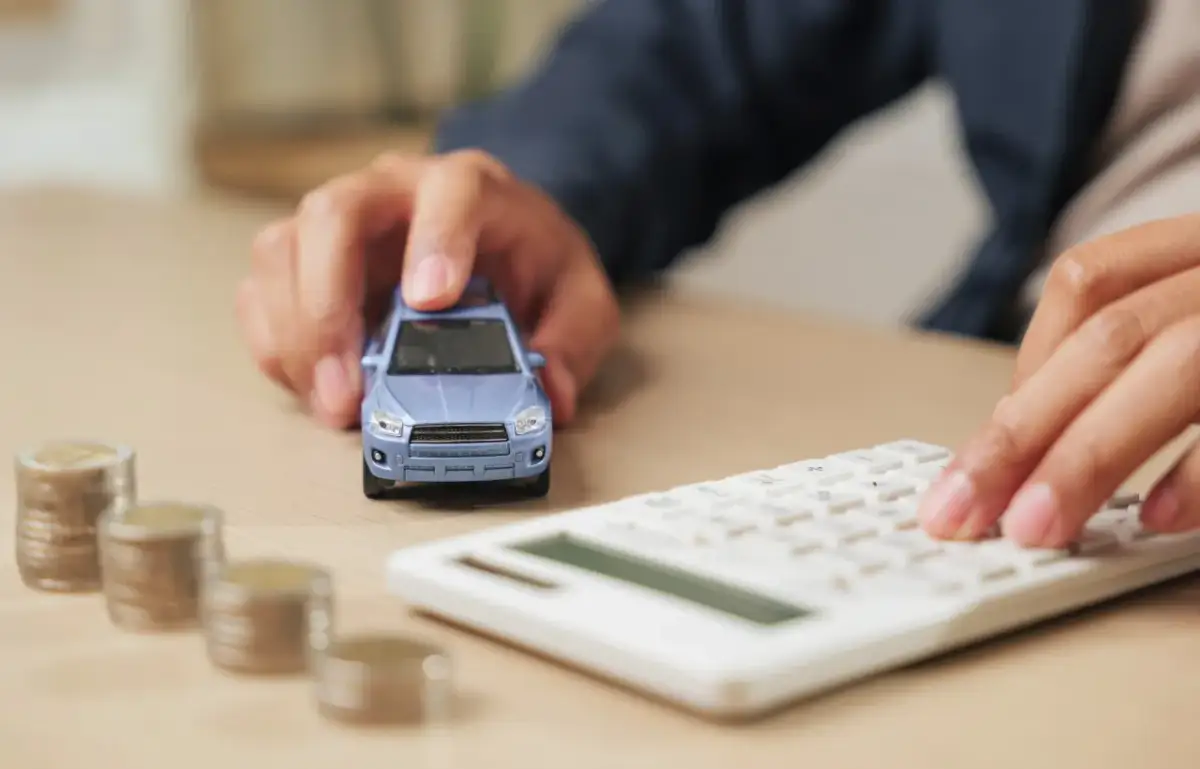 Ręka przesuwa niebieski samochodzik obok stosów monet i kalkulatora. Czy bocian sprawdza bik?