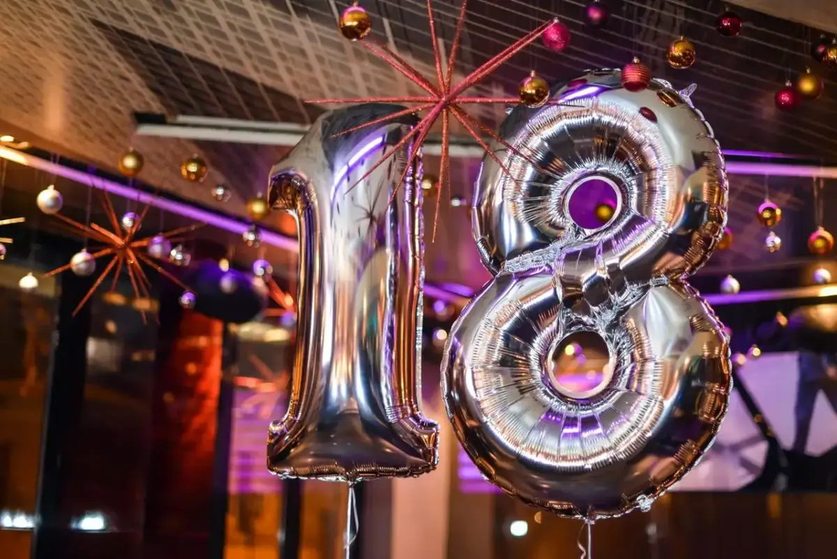 Srebrne balony z cyfrą 18 wiszą wśród ozdób. Idealne na imprezę, zastanawiasz się, ile dajemy na osiemnastkę?