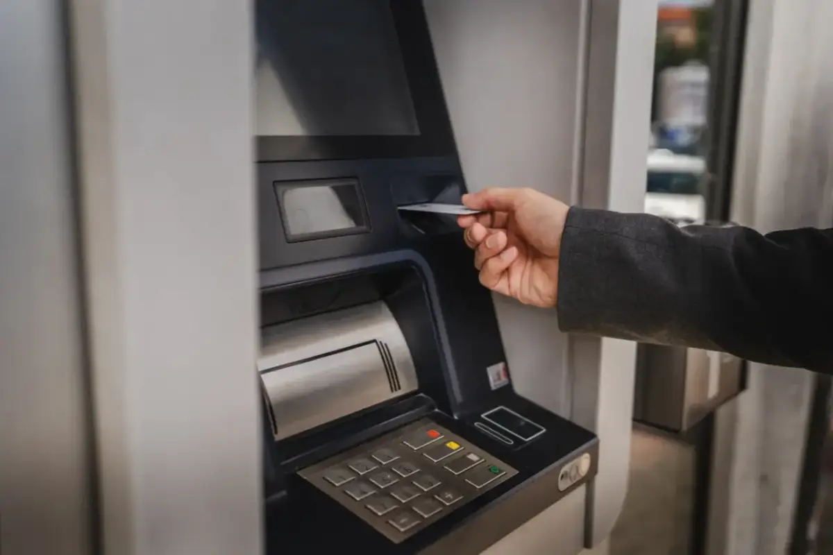 Dłoń wsuwa kartę do bankomatu, by sprawdzić, ile można wypłacić.
