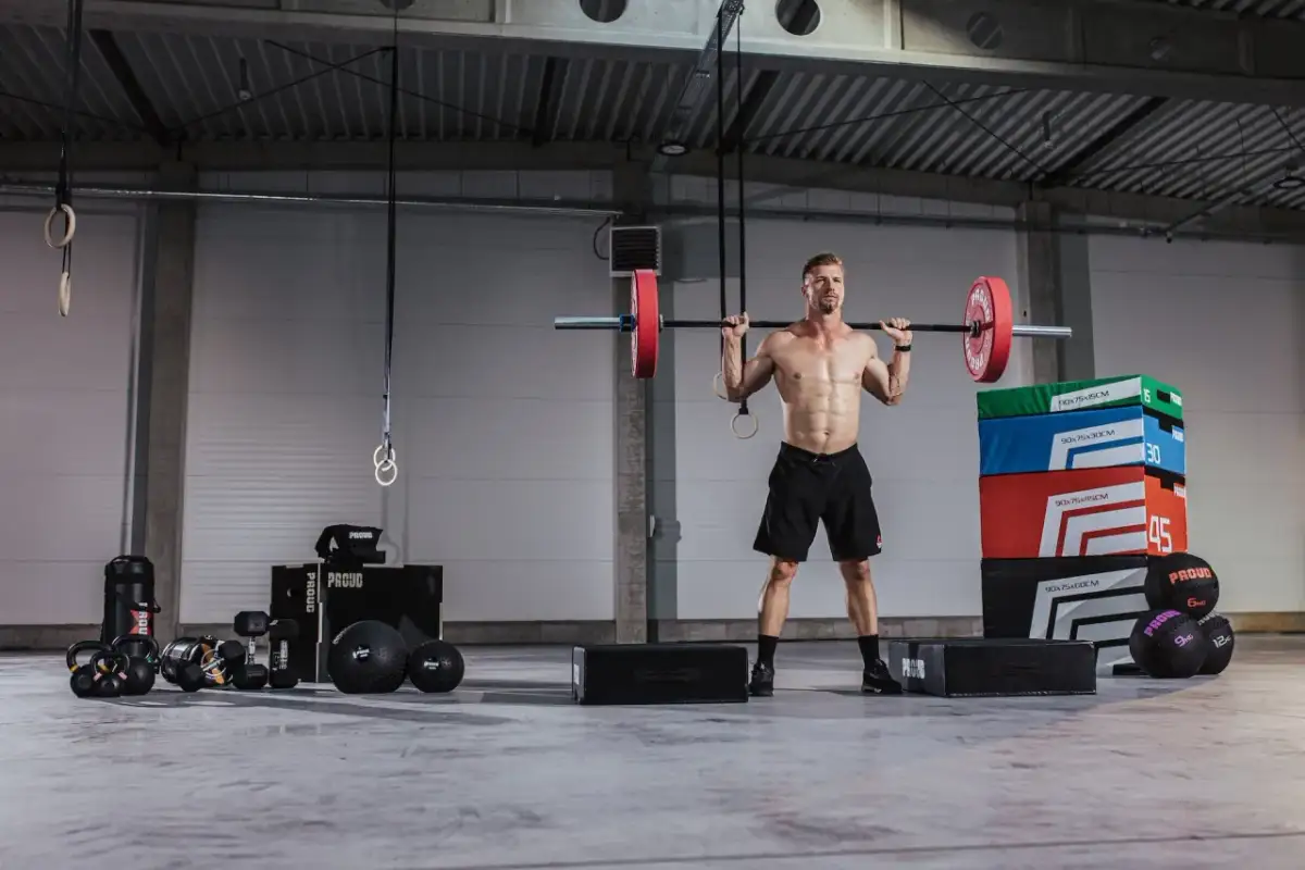 Siłownia pełna sprzętu do treningu. Mężczyzna z idealnym brzuchem podnosi sztangę. To inspiracja, jakie ćwiczenia na brzuch na siłowni wybrać.