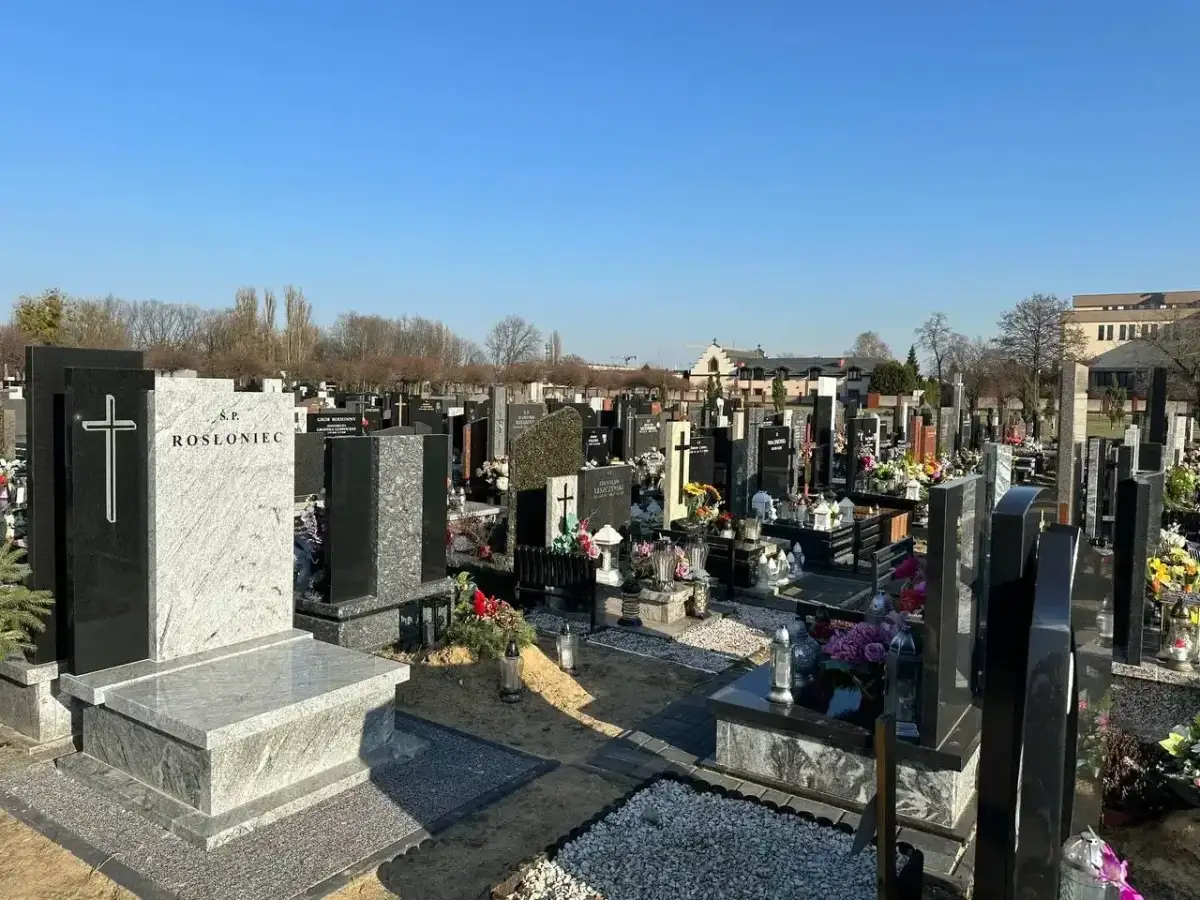 Nagrobek z krzyżem i napisem "Ś.P. ROSŁoniec" na tle cmentarza.