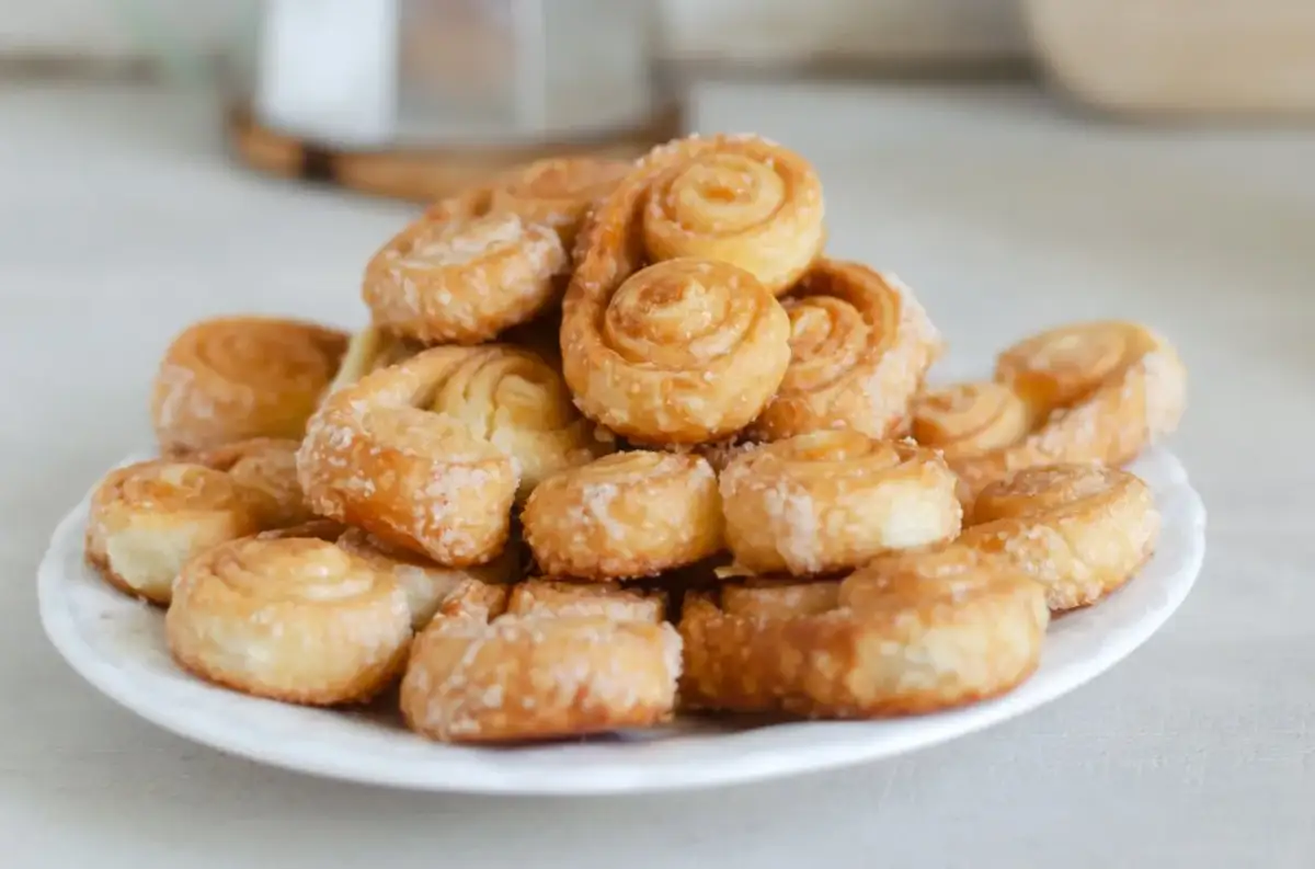Stos ciasteczek z ciasta francuskiego, posypanych cukrem, na białym talerzu. Idealne na deser!