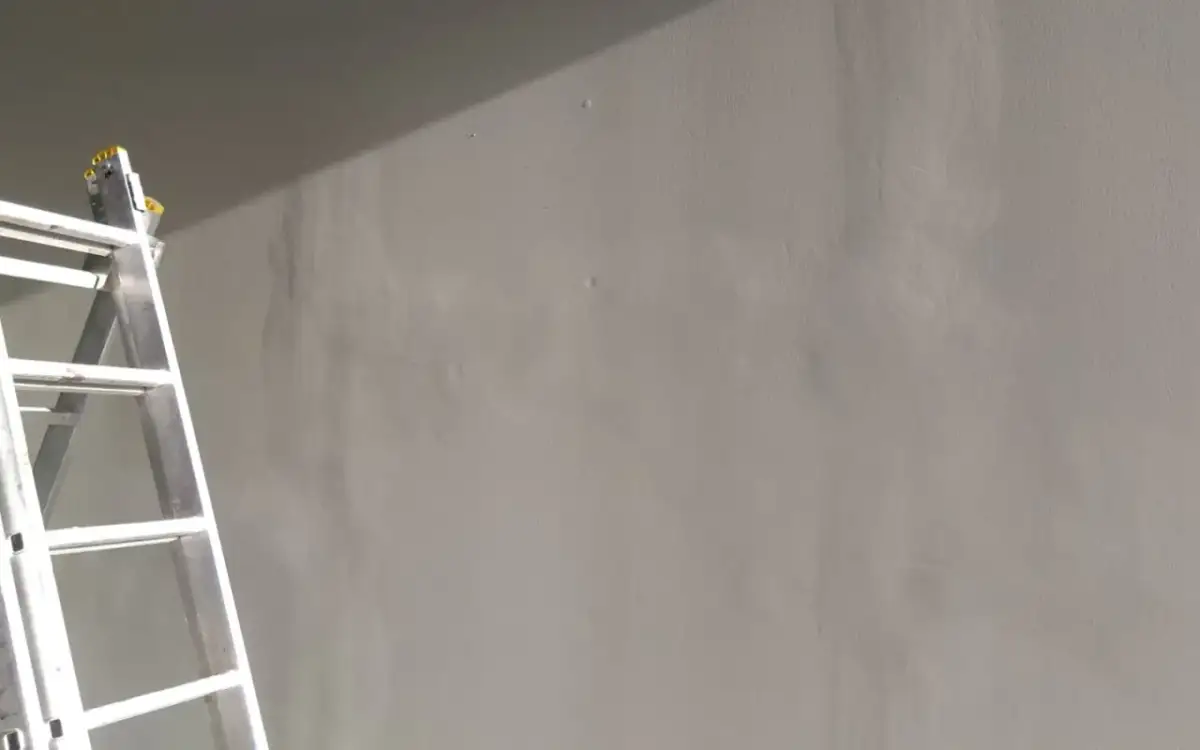 Drabina przy szarej ścianie. Pytanie brzmi: czy można malować płytę GK bez gładzi? Odpowiedź wkrótce.