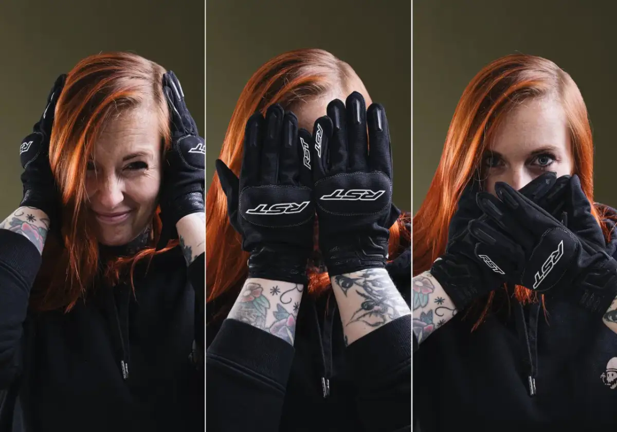 Kobieta z rudymi włosami w czarnych rękawicach motocyklowych zakrywa twarz.