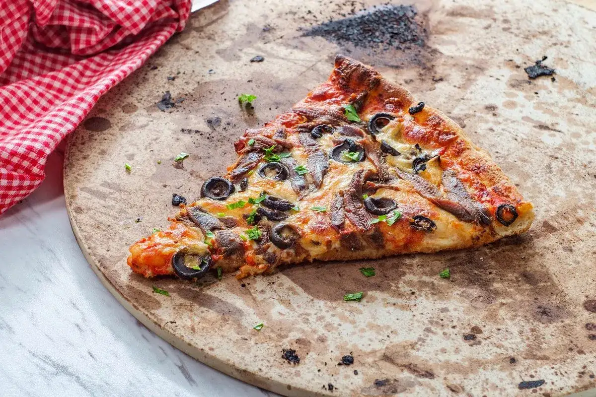 Kawałek pizzy z anchois i oliwkami na kamieniu. Dowiedz się, jak wyczyścić kamień do pizzy, by był jak nowy.